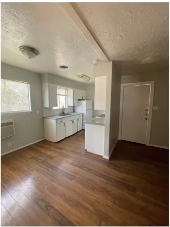 an empty room with wooden floor kitchen view and windows