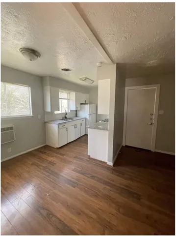 an empty room with wooden floor kitchen view and windows