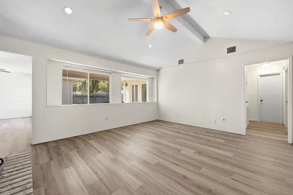 an empty room with wooden floor chandelier fan and windows