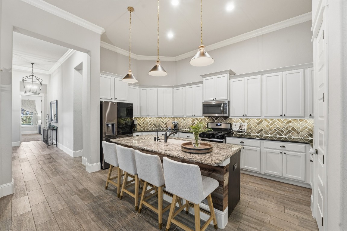 2172 Rope Maker Road Conroe, TX 77384 - Photo 13 of 50 This spacious kitchen features elegant white cabinetry, a central island with granite countertops, and modern stainless-steel appliances. The room is well-lit with pendant lighting and has a stylish herringbone brick backsplash that ties nicely into the living room fireplace.
