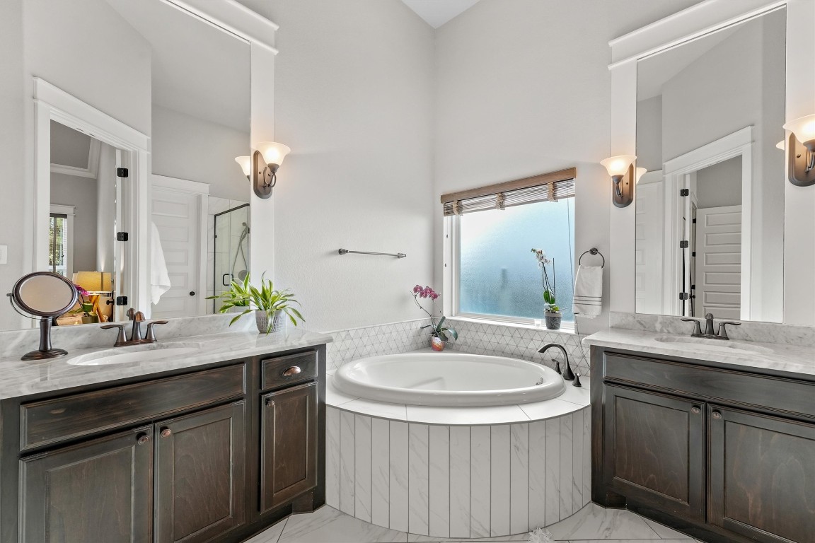 2172 Rope Maker Road Conroe, TX 77384 - Photo 22 of 50 Primary bathroom features a spacious, elegant design with a central soaking tub, dual vanities with marble countertops, and dark wood cabinetry. It includes modern fixtures, ample natural light from a frosted window, and stylish wall sconces.