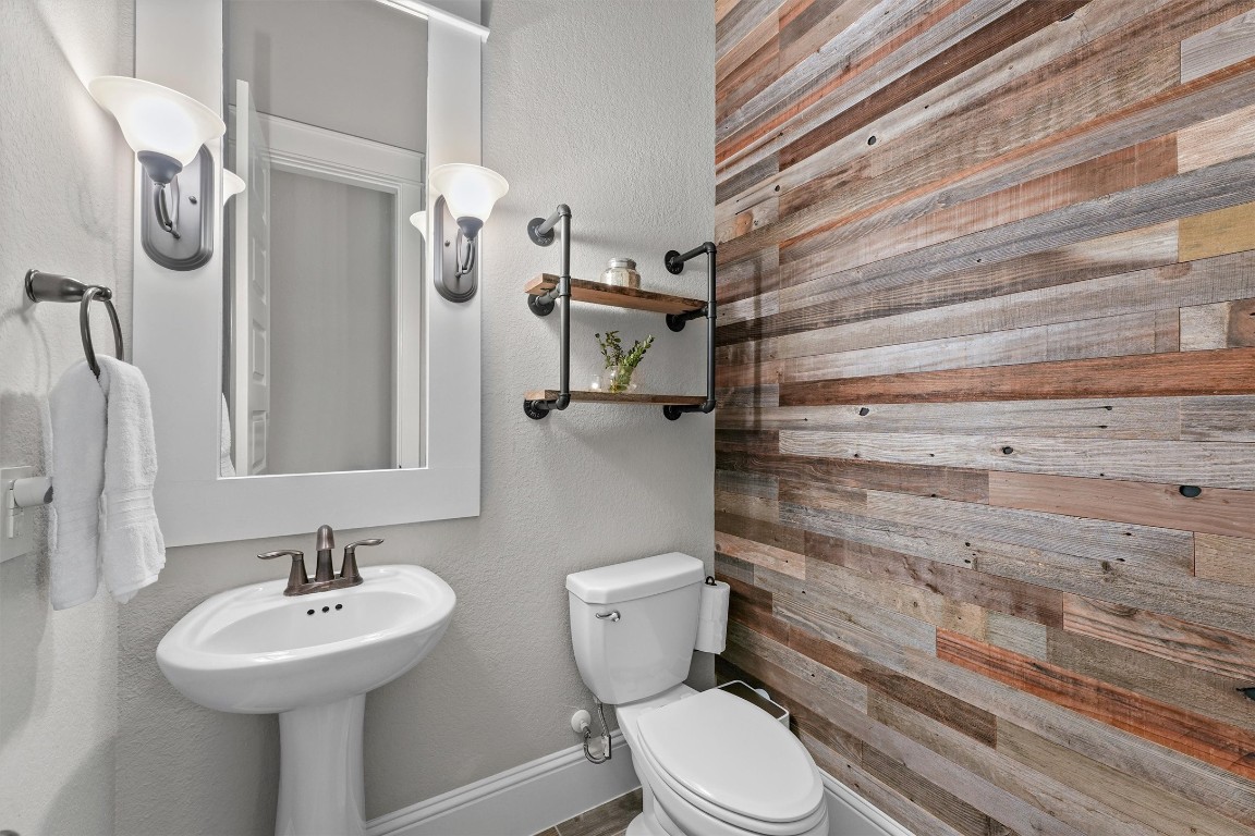 2172 Rope Maker Road Conroe, TX 77384 - Photo 26 of 50 Half bathroom features a stylish wood plank accent wall, a pedestal sink, and modern light fixtures. It has a clean, contemporary design with open shelving and neutral tones for a cozy, inviting atmosphere.