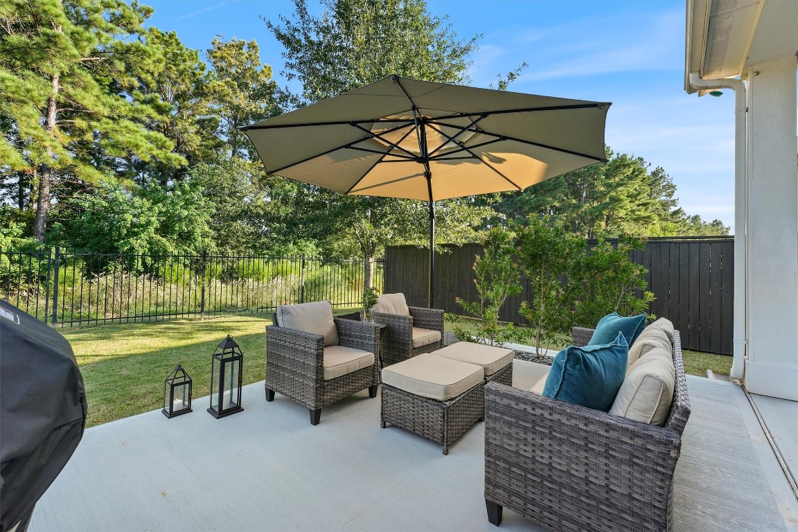 2172 Rope Maker Road Conroe, TX 77384 - Photo 34 of 50 Charming backyard patio with stylish outdoor seating, a large umbrella for shade, and lush greenery.