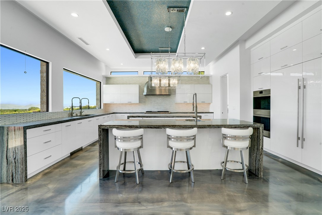 10 Ridge Blossom Road Las Vegas, NV 89135 - Photo 11 of 69 Kitchen with dark stone counters, finished concrete flooring, a center island with sink, white cabinets, and backsplash