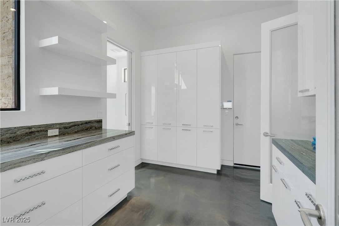 10 Ridge Blossom Road Las Vegas, NV 89135 - Photo 15 of 69 Large Butler's pantry with open shelves, white cabinets, concrete flooring, and dark stone counters.