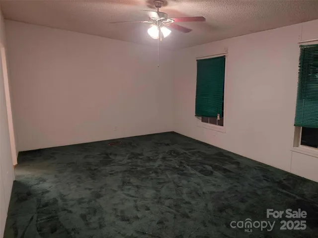 a view of an empty room with window and chandelier fan