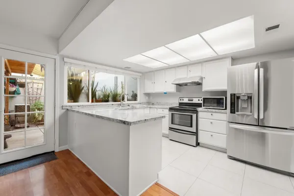 a kitchen with granite countertop a refrigerator oven a sink dishwasher and white cabinets next to a window