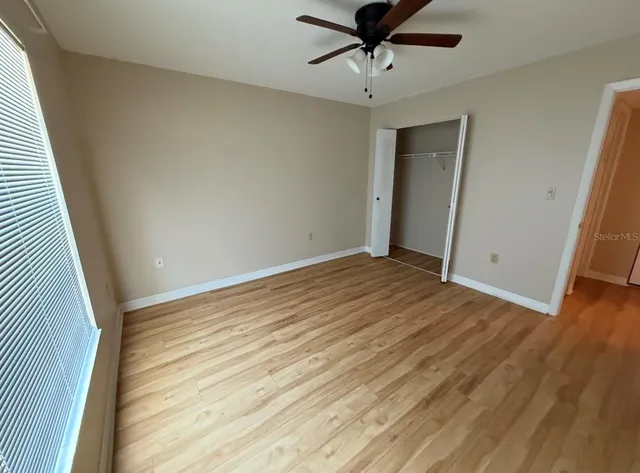 an empty room with wooden floor fan and windows
