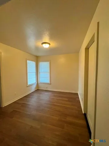 a view of a refrigerator in kitchen and an empty room in wooden floor