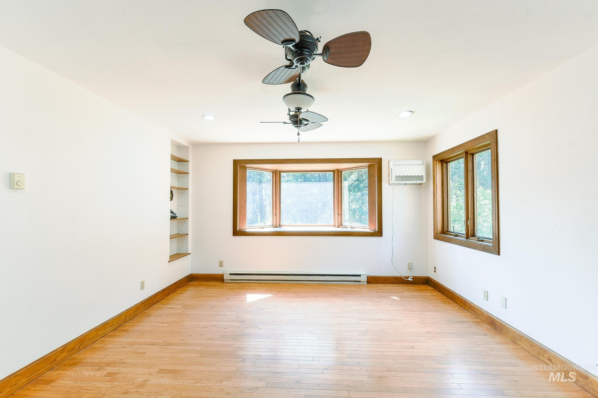 Hardwood flooring with natural wood trim, bay window with built-in bench, recessed lighting, and dual ceiling fans