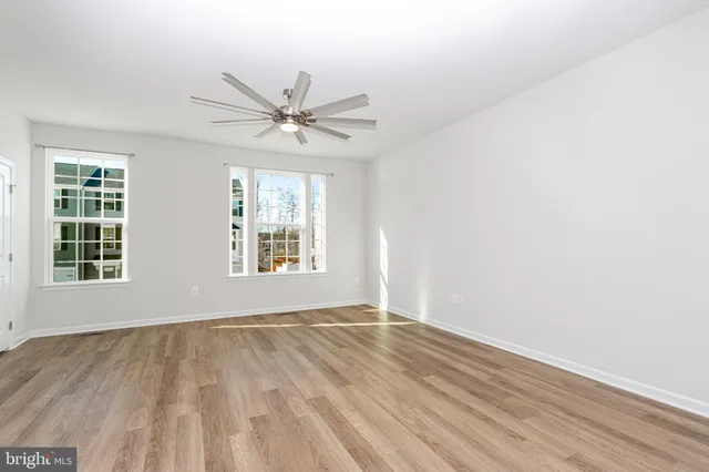 an empty room with wooden floor fan and windows