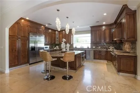 a kitchen with stainless steel appliances kitchen island granite countertop a refrigerator a sink dishwasher a stove and a dining table with wooden cabinet