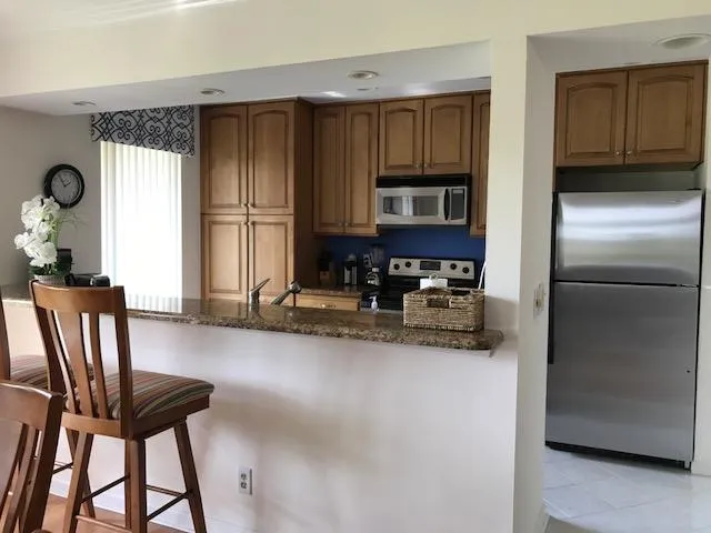 a kitchen with stainless steel appliances granite countertop a refrigerator a stove a sink a dining table and chairs with wooden floor