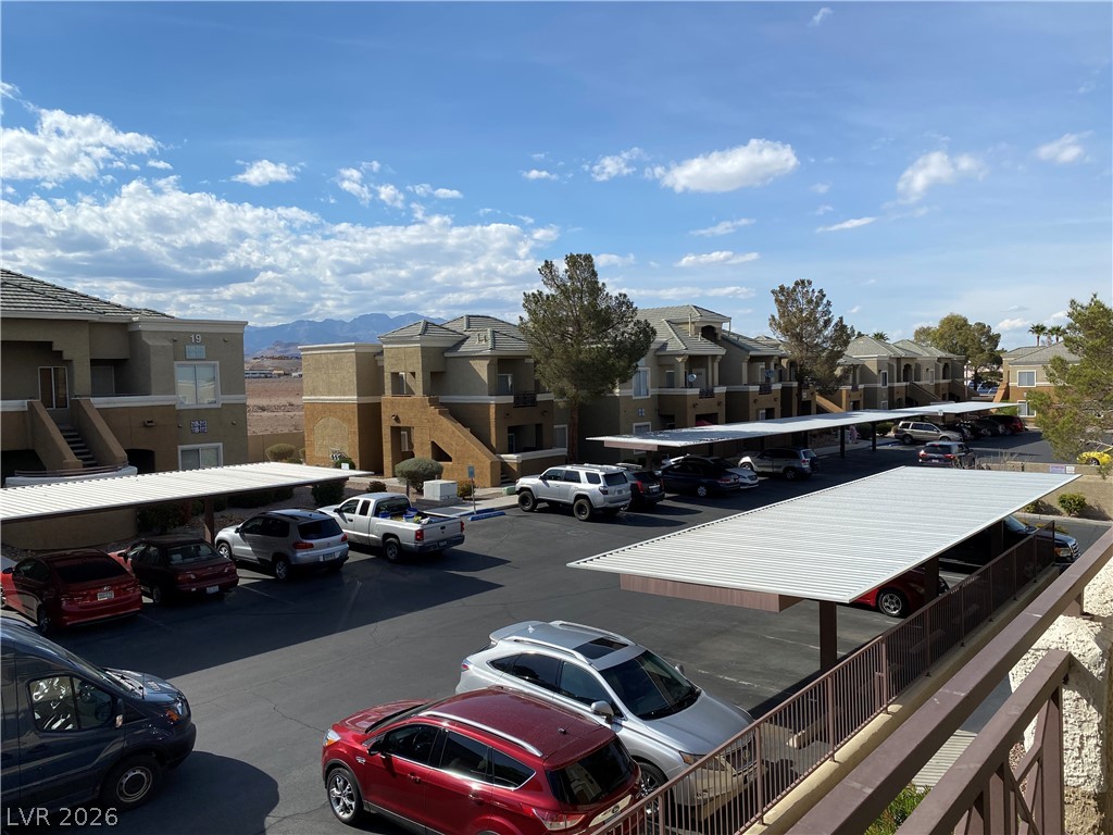 8070 West Russell Road, Unit 2105 Las Vegas, NV 89113 - Photo 1 of 10 Ample covered parking spaces serve multi-level residential structures under a vast sky, with distant mountains providing a scenic backdrop.