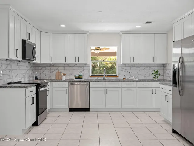 a large white kitchen with a stove a sink dishwasher and a refrigerator with white cabinets