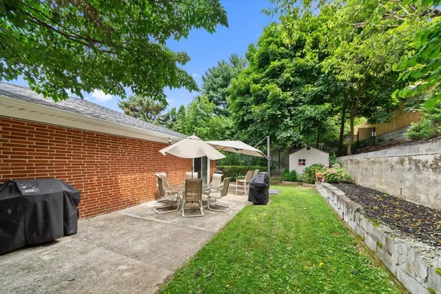 a view of a patio with table and chairs under an umbrella with large trees