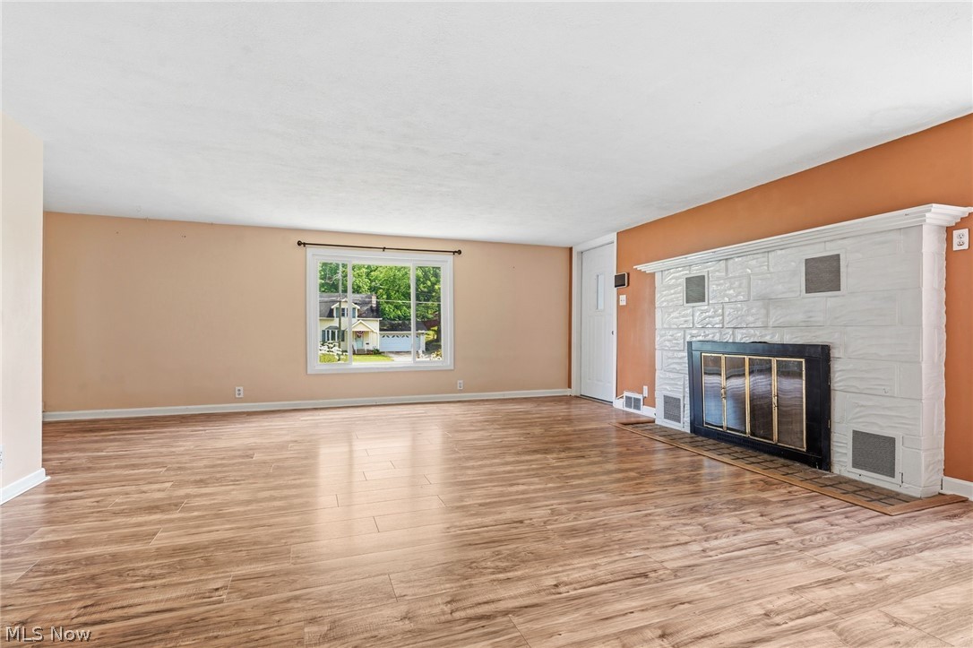 4449 18th Street Northwest Canton, OH 44708 - Photo 7 of 25 Spacious interior room featuring wood-finish flooring, a white brick fireplace with a black firebox, a large window, and an entry door