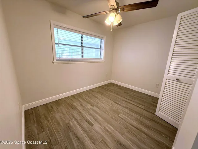 an empty room with wooden floor fan and windows