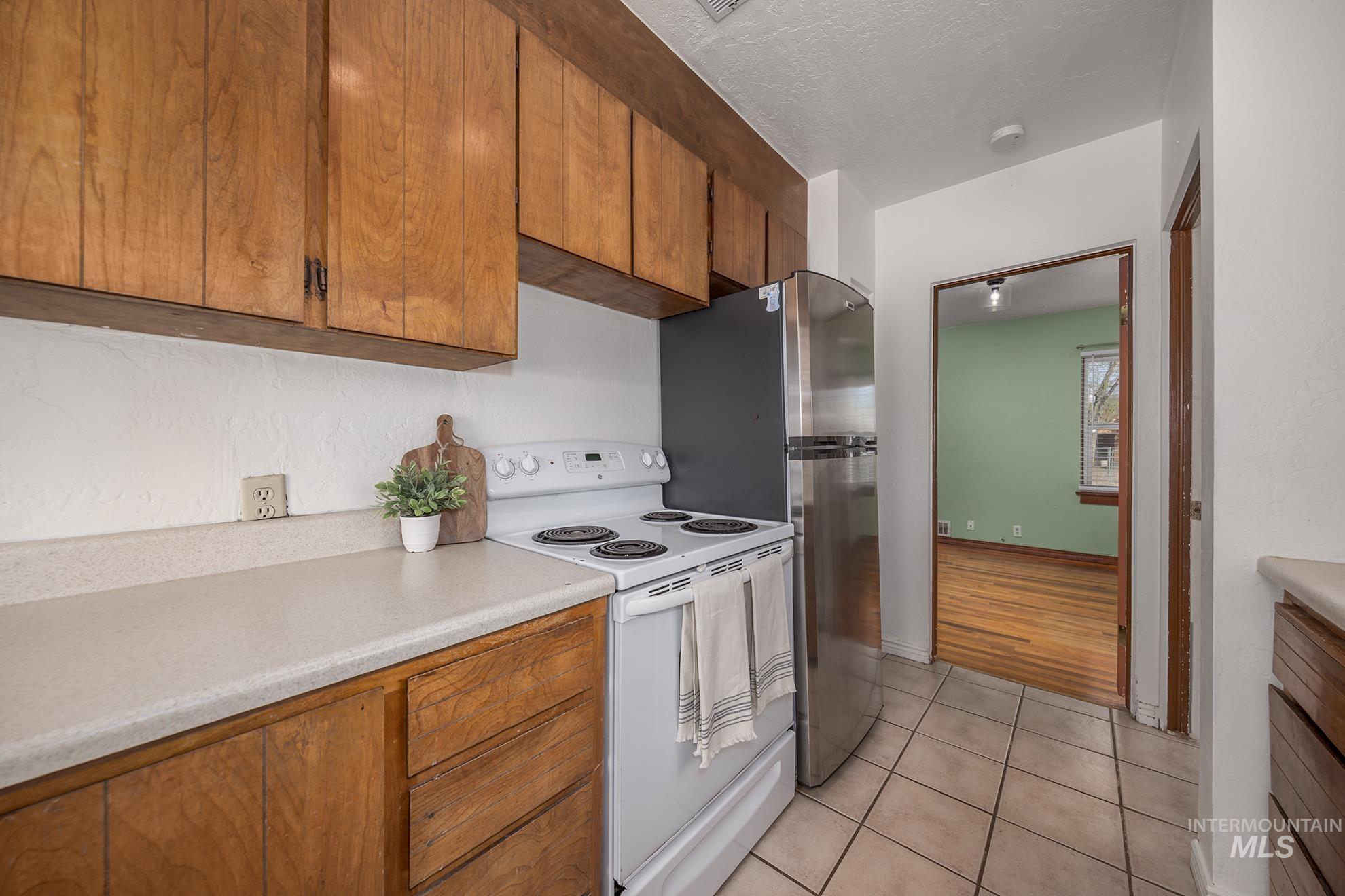 1016 West 5th Street Weiser, ID 83672 - Photo 8 of 36 Kitchen with white electric range, wood finish cabinets, light countertops, light tile patterned flooring, and a textured ceiling