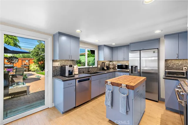 a kitchen with stainless steel appliances kitchen island granite countertop a stove top oven a sink dishwasher a dining table and chairs with wooden floor