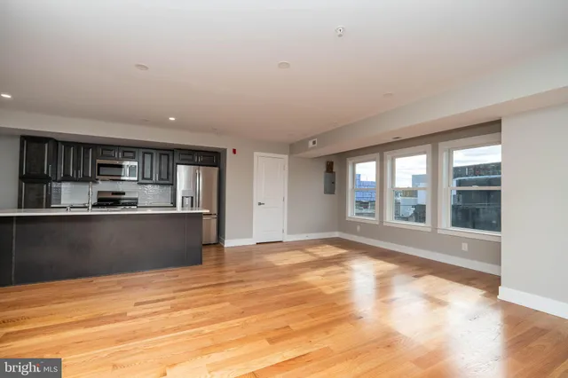 a view of empty room with wooden floor and kitchen view