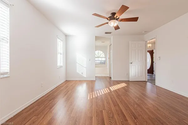 an empty room with wooden floor fan and windows