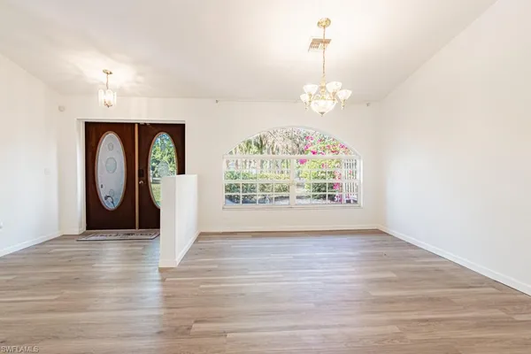 an empty room with wooden floor chandelier and windows