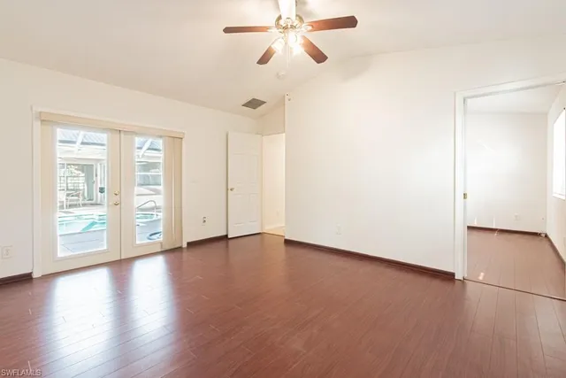 an empty room with wooden floor chandelier fan and windows