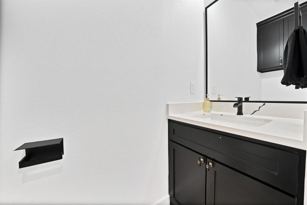 805 Tierney Road Fort Worth, TX 76112 - Photo 21 of 36 Built-in vanity with dark cabinetry, white countertop, integrated sink, and a black framed mirror
