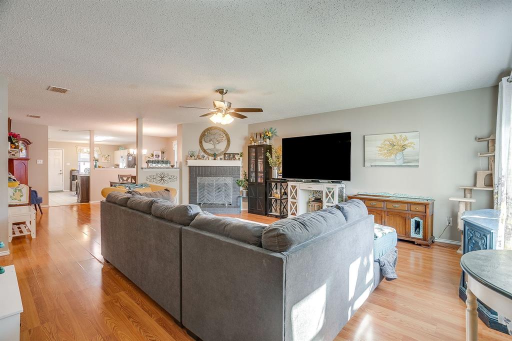 Living area featuring wood-finish flooring, a ceiling fan, and a fireplace with a dark gray brick surround and a white mantel