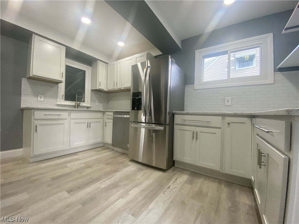12913 Silver Road Cleveland, OH 44125 - Photo 7 of 23 Kitchen with backsplash, white cabinets, vaulted ceiling, light countertops, light hardwood flooring, and stainless steel appliances