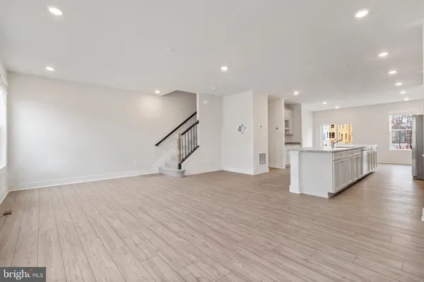 a view of an empty room with wooden floor and a kitchen