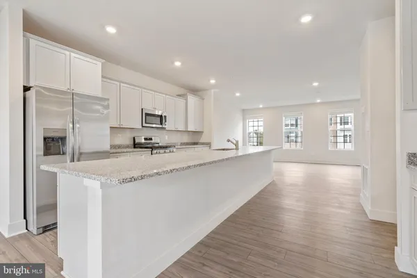 a view of kitchen with stainless steel appliances granite countertop a stove a sink a refrigerator and white cabinets with wooden floor