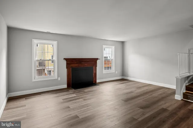 an empty room with wooden floor fireplace and windows