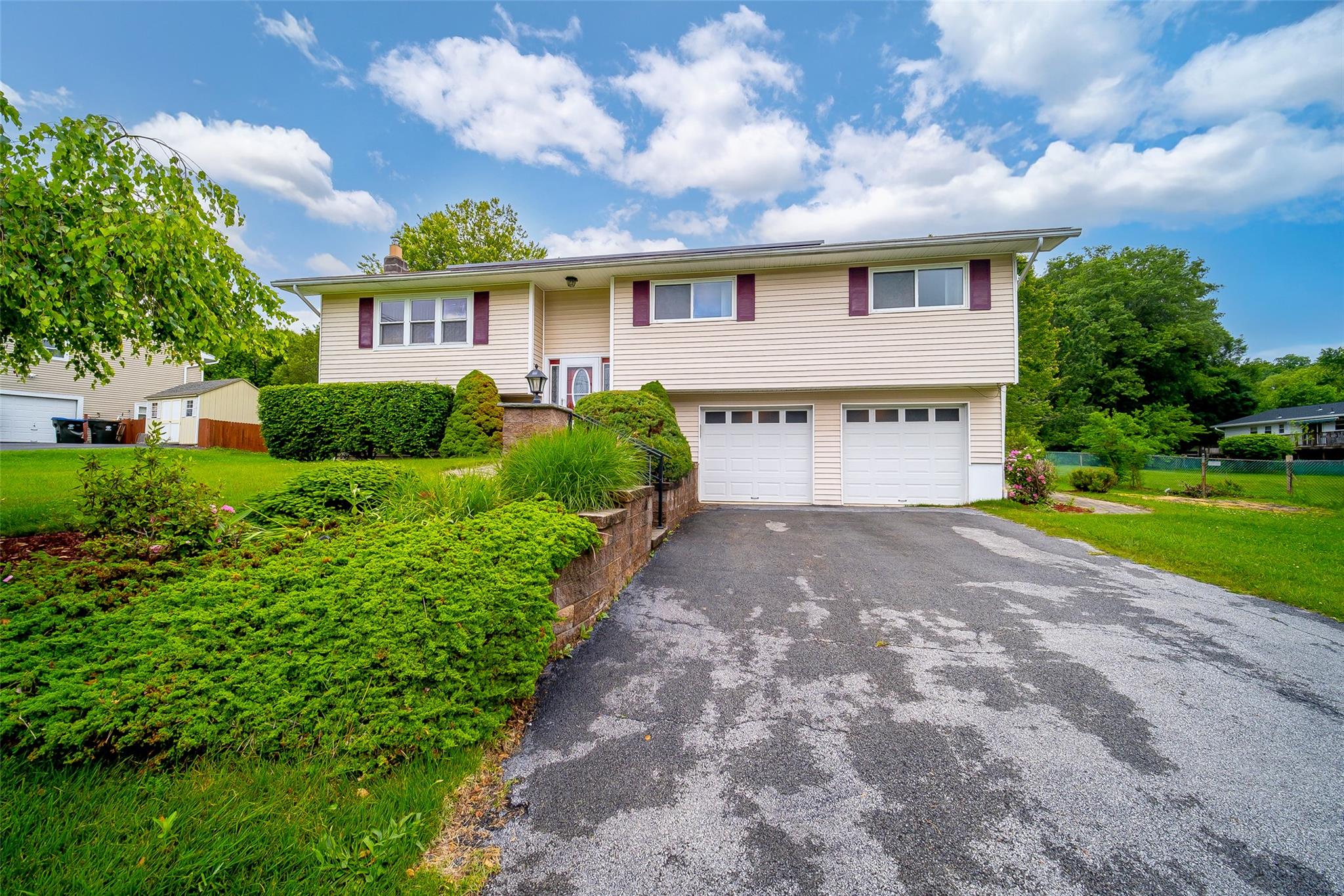 Raised ranch with asphalt driveway, a two-car garage, and a parklike entrance.
