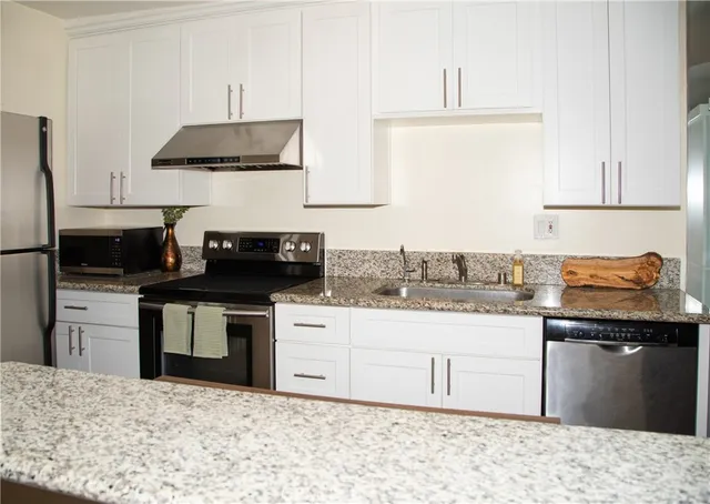 a kitchen with stainless steel appliances kitchen island granite countertop a stove top oven a sink a counter space and cabinets