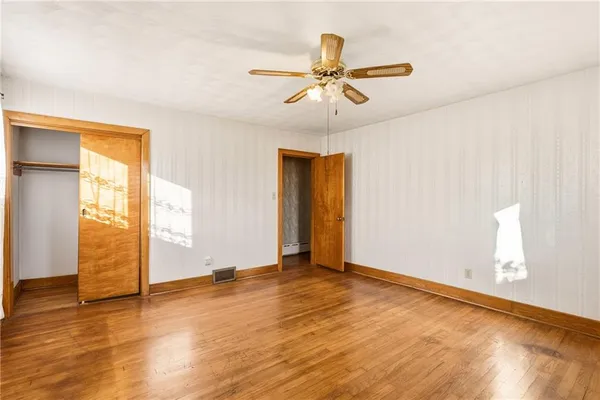 a view of an empty room with wooden floor and a ceiling fan
