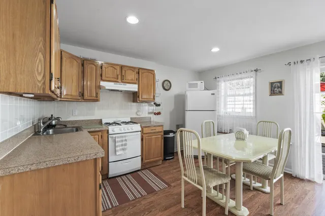 a kitchen with stainless steel appliances granite countertop a stove top oven a sink dishwasher and a refrigerator with wooden floor