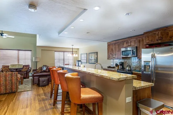 a dining room with stainless steel appliances granite countertop a refrigerator a stove top oven a dining table and chairs with wooden floor
