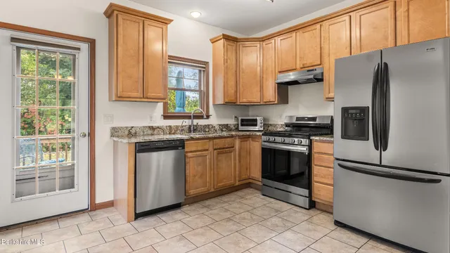 a kitchen with stainless steel appliances granite countertop a refrigerator a sink a stove top oven and a window