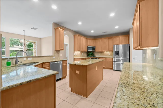 a large kitchen with kitchen island granite countertop a large counter top stainless steel appliances a sink a window and cabinets
