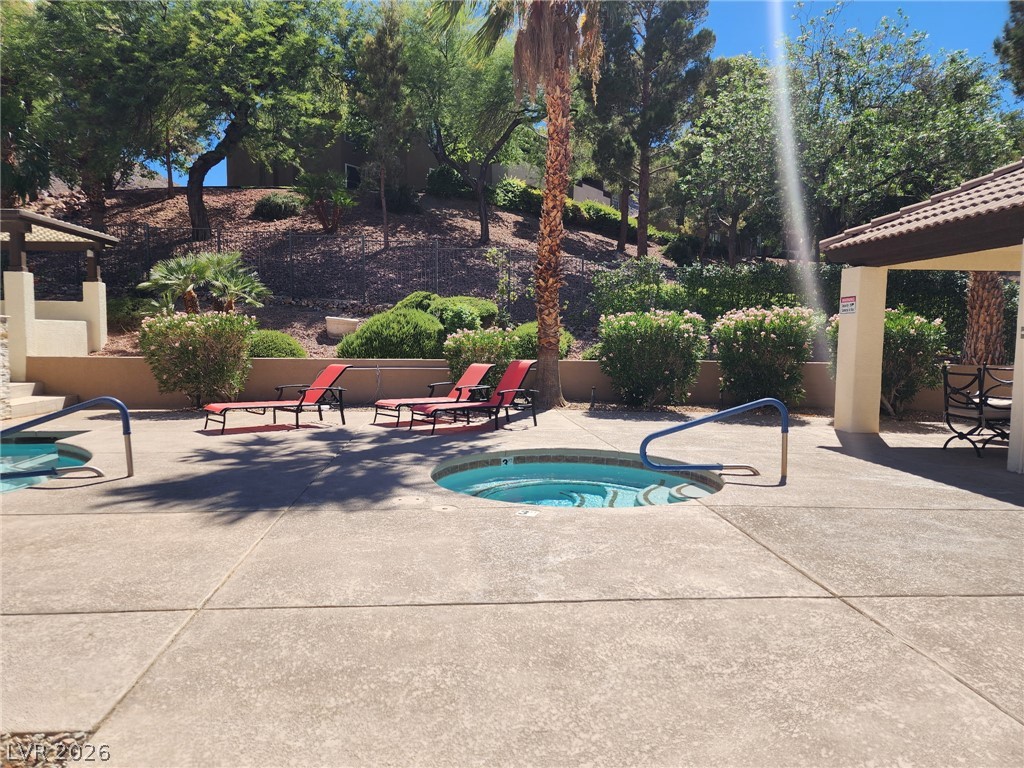 231 West Horizon Ridge Parkway, Unit 1127 Henderson, NV 89012 - Photo 39 of 39 An inviting outdoor space featuring a hot tub and relaxation loungers, surrounded by lush, mature landscaping.