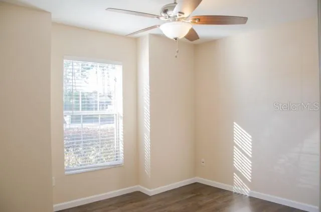 an empty room with wooden floor fan and windows