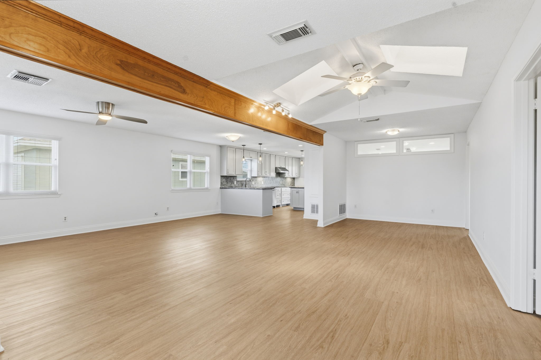 119 Sand Shoals Road Freeport, TX 77541 - Photo 16 of 34 Open-concept living and dining — vaulted ceiling with exposed natural wood beam, dual ceiling fans, skylight, and light wood-look LVP flooring flowing into the kitchen.