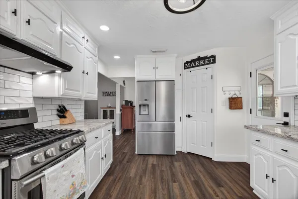 a kitchen with granite countertop a refrigerator a stove and white cabinets with wooden floor