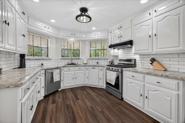 a kitchen with granite countertop white cabinets white appliances a sink and a window