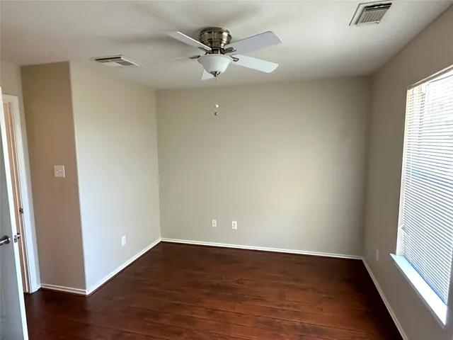 an empty room with wooden floor fan and windows