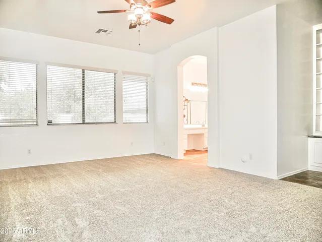 an empty room with chandelier fan and windows