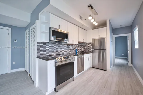 a kitchen with stainless steel appliances granite countertop a stove top oven a refrigerator cabinets and wooden floor