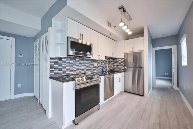 a kitchen with stainless steel appliances granite countertop a stove top oven a refrigerator cabinets and wooden floor